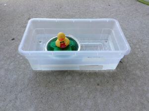 A "lock" made from a plastic "shoe box", with water levels marked with tape and marker on the side. The water is currently at the "low" level, with a demonstration "boat" floating the cargo and a quacky passenger.